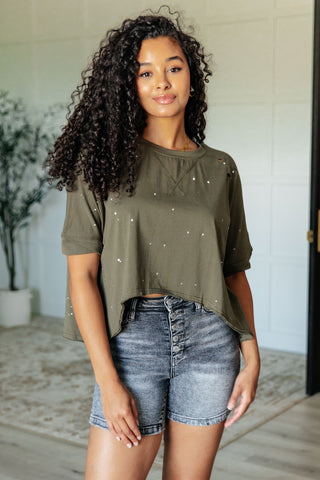 Woman wearing an olive green asymmetrical top with paint splatter design 