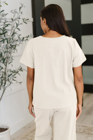 Rear view of woman wearing a plain cream t-shirt and pants in an indoor setting with a plant.