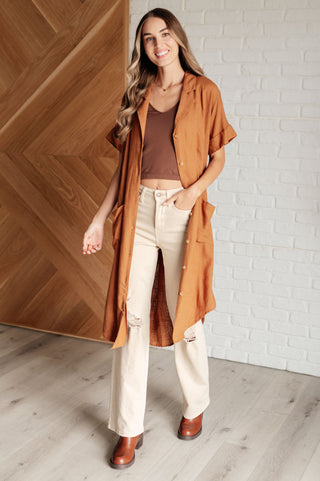Woman wearing a long brown shirt dress as a duster over a brown top and white pants.