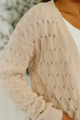 Close-up of a beige cable knit cardigan with a blurred background