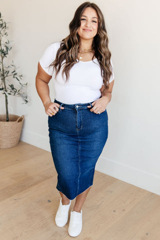 Beautiful plus sized model wearing a white t-shirt and blue denim skirt standing indoors.