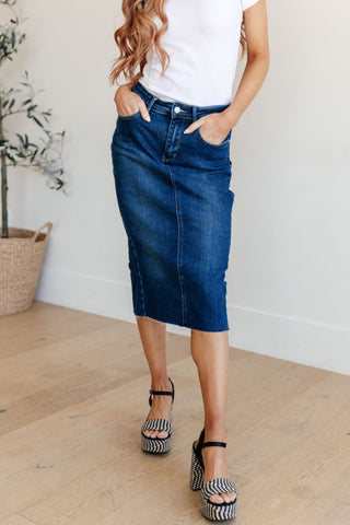 Woman wearing a dark blue denim skirt and white top indoors.