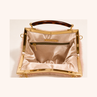 A kiss clasp frame handbag with a glossy gold-tone metal frame, a brown tortoiseshell inspired top handle, and a light faux fur exterior. The interior is lined with champagne satin, featuring a zippered pocket and a gold-tone brand plaque.