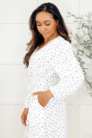 Side view of woman wearing a white maple leaf print long-sleeve dress in a minimalistic setting.