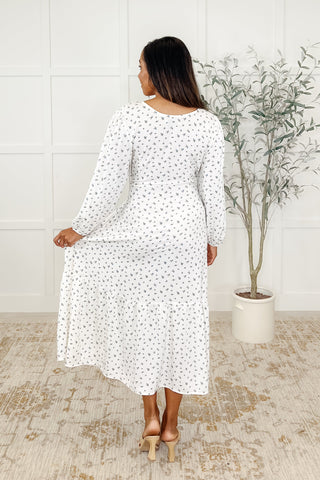 Rear view of woman wearing a white dress with small maple leaf patterns in a room with a plant and tiled floor.