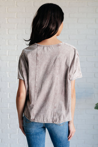 Rear view of person wearing a beige t-shirt and blue jeans against a white brick wall.