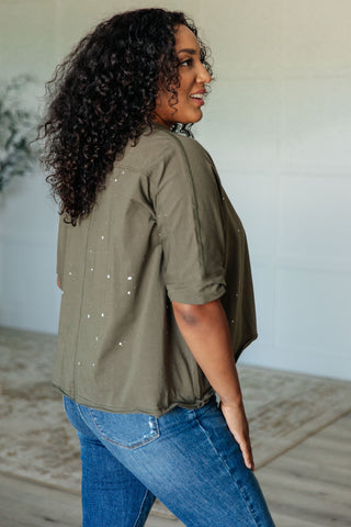Three quarter view of woman wearing an olive green top and blue jeans standing indoors.
