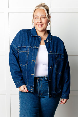 Plus sized model wearing a blue denim jacket and jeans against a white tiled wall.