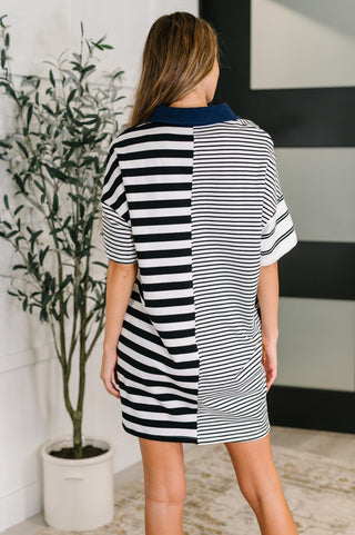 Rear view of woman wearing a black and white striped dress standing in a room with a plant and wall art.