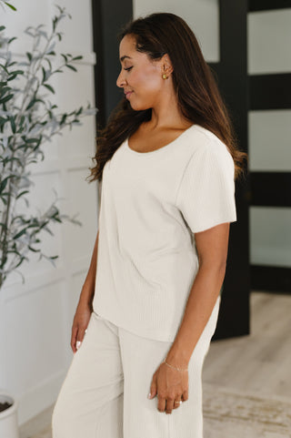 Side view of woman wearing soft beige tee standing indoors with a plant in the background