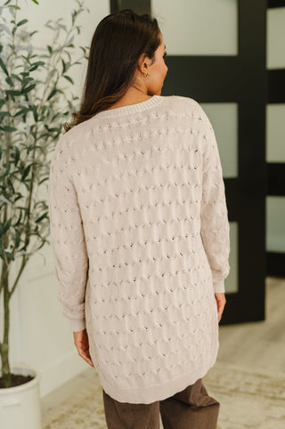 Rear view of tan cable knit cardigan on female model in an indoor setting