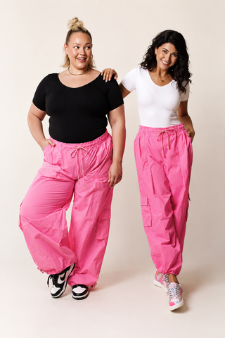 Two women wearing pink cargo pants and black and white tops on a plain background