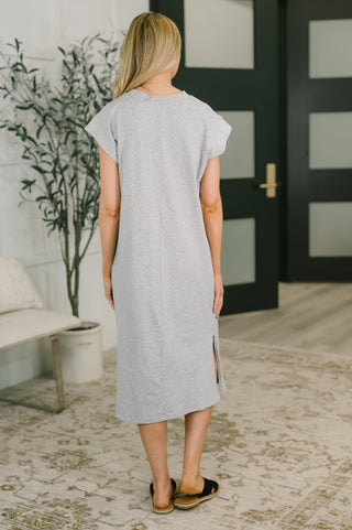 Rear view of woman wearing a gray dress standing in a room with a plant and door in the background