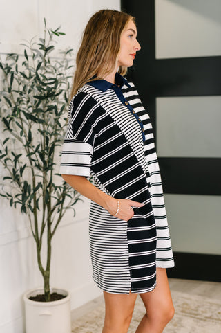 Side view of woman wearing a black and white striped dress with navy blue collar standing next to a potted plant indoors.