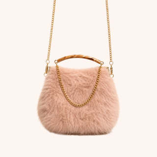 A light pink faux fur handbag with a gold chain strap and a curved resin handle, shown against a solid off-white background.