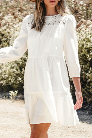 Woman standing outdoors wearing a cotton and lyocell white dress with lace details and a wide-brimmed hat on a plain background